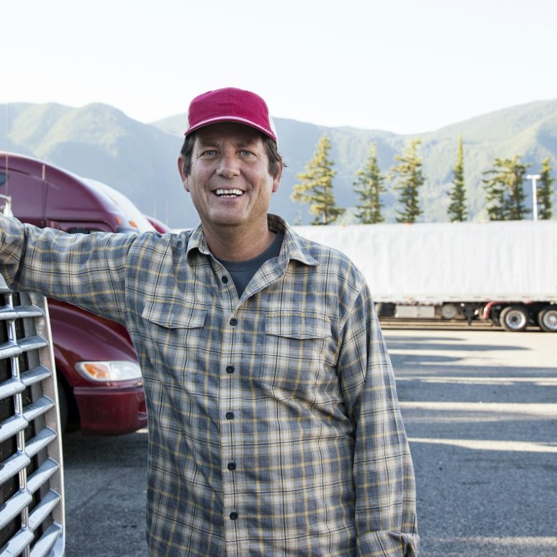 Caucasian man truck driver with his truck parked in a lot at a truck stop.